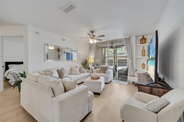 living area with ceiling fan, light wood finished floors, and a textured ceiling