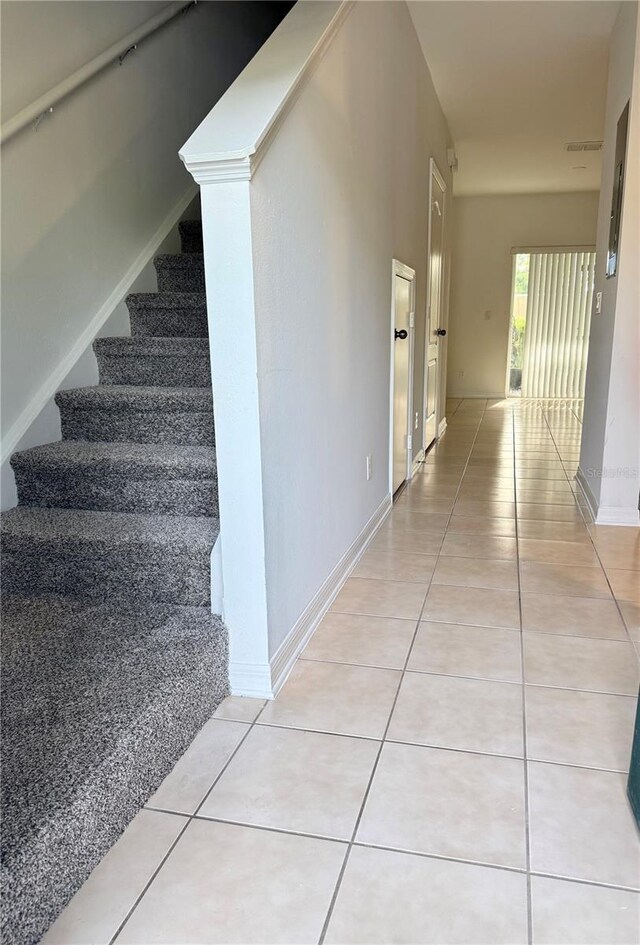 corridor featuring stairway, light tile patterned floors, and baseboards