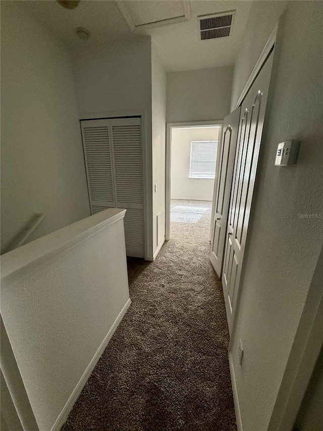 corridor featuring dark carpet, baseboards, and a textured wall