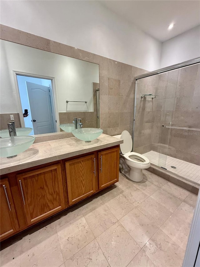 bathroom with a shower stall, double vanity, toilet, and tile walls