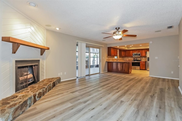2006 Sycamore Ln, Plant City, FL 33563 - unfurnished living room with ceiling fan, light wood-style floors, a textured ceiling, baseboards, and a large fireplace