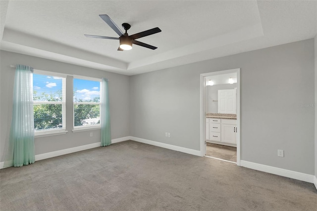 15975 Marina Bay Dr, Winter Garden, FL 34787 - unfurnished bedroom with a tray ceiling, light colored carpet, baseboards, and ensuite bath