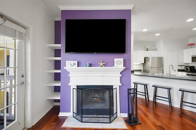 living room featuring dark wood finished floors, crown molding, recessed lighting, a fireplace with flush hearth, and built in features