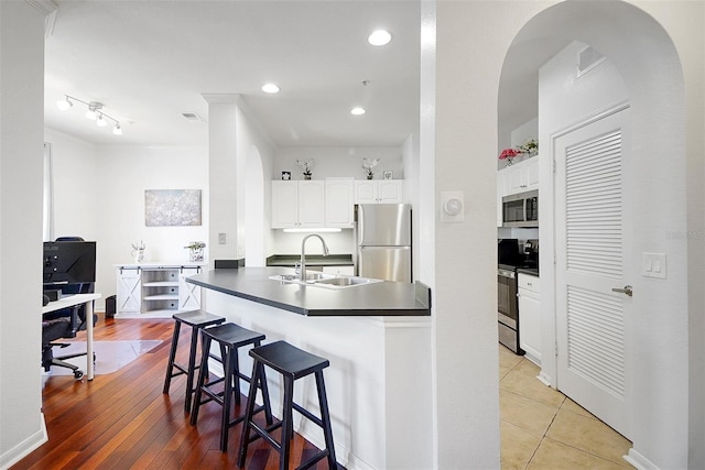 kitchen with appliances with stainless steel finishes, a sink, dark countertops, a breakfast bar area, and white cabinets