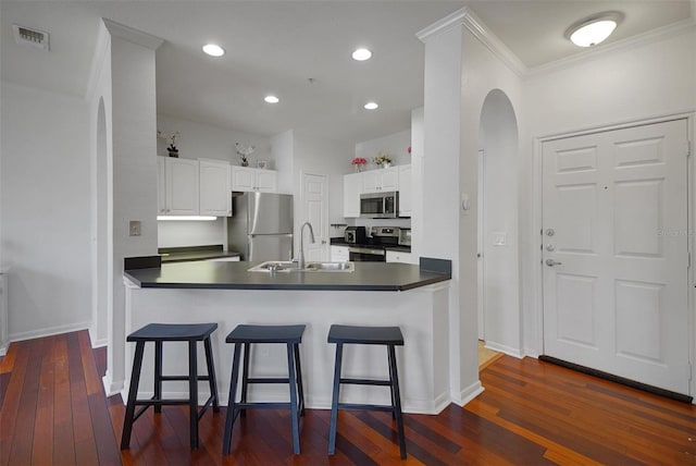 kitchen featuring stainless steel appliances, a sink, arched walkways, dark countertops, and crown molding