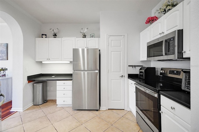 kitchen featuring stainless steel appliances, dark countertops, arched walkways, white cabinetry, and light tile patterned flooring
