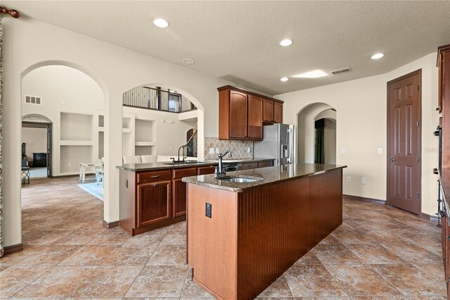 3041 Boating Blvd, Kissimmee, FL 34746 - kitchen featuring stainless steel refrigerator with ice dispenser, a sink, dark stone counters, arched walkways, and a textured ceiling