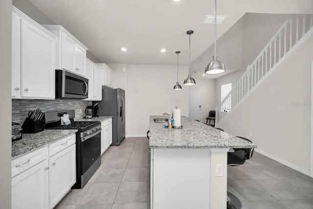 kitchen featuring appliances with stainless steel finishes, tasteful backsplash, an island with sink, baseboards, and a breakfast bar