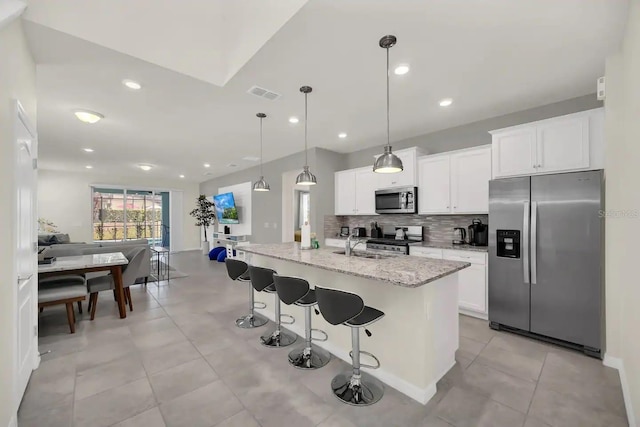 kitchen with appliances with stainless steel finishes, backsplash, light stone countertops, a kitchen breakfast bar, and white cabinets