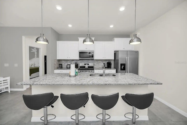 kitchen with appliances with stainless steel finishes, a sink, a kitchen island with sink, tasteful backsplash, and white cabinets