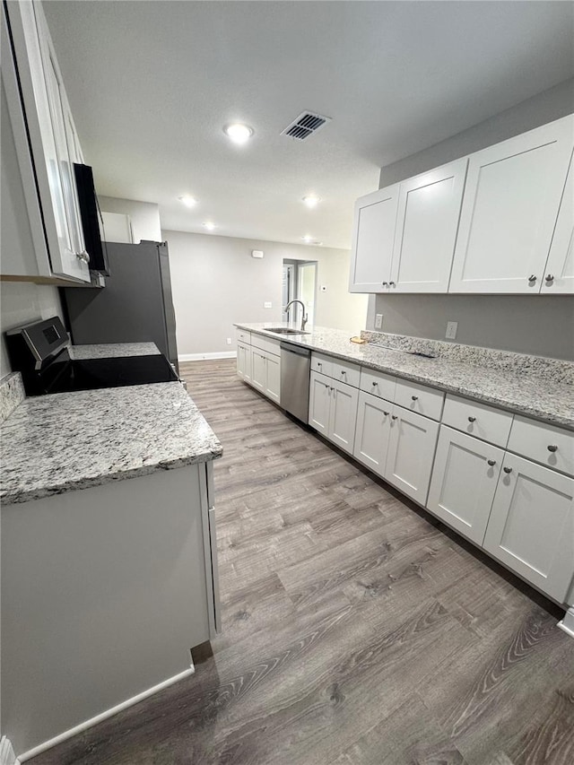 kitchen featuring stainless steel appliances, light wood-type flooring, a peninsula, white cabinets, and baseboards