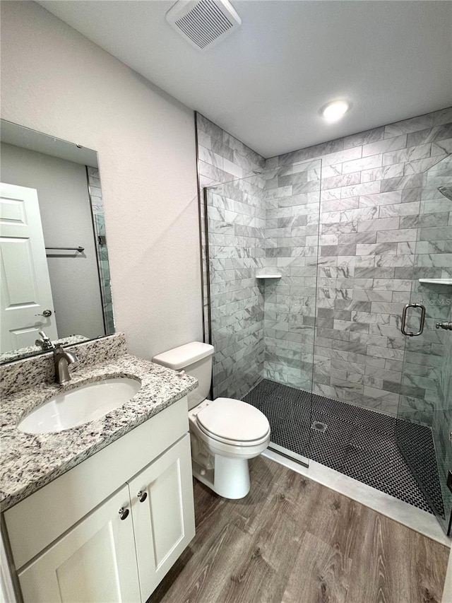 bathroom featuring wood finished floors, a stall shower, toilet, and vanity