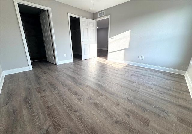 unfurnished bedroom featuring wood finished floors, baseboards, a closet, and a walk in closet