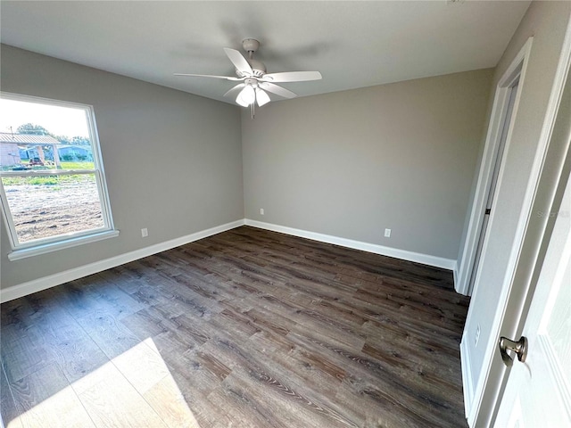 unfurnished room with dark wood finished floors, a ceiling fan, and baseboards