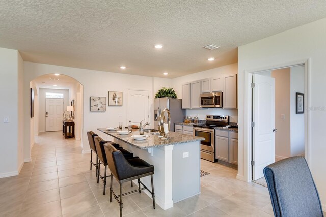 5169 Masser Rd, Saint Cloud, FL 34772 - kitchen featuring appliances with stainless steel finishes, gray cabinets, a center island with sink, arched walkways, and a kitchen breakfast bar