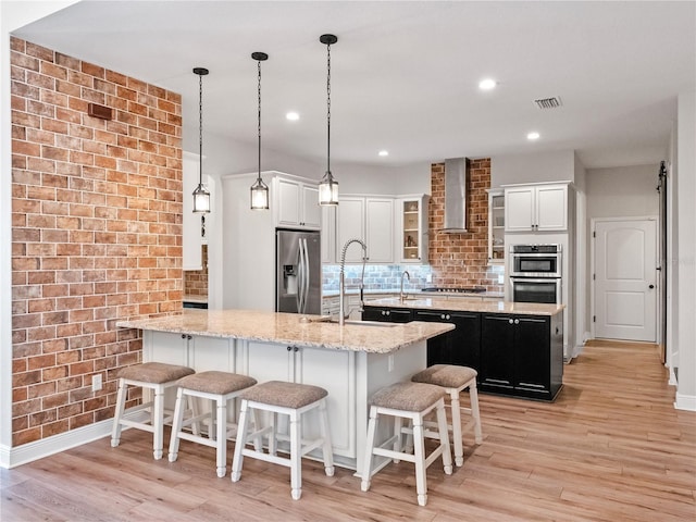 20199 Sweetwood Ln, Clermont, FL 34715 - kitchen featuring stainless steel appliances, wall chimney range hood, a sink, a kitchen island with sink, and light wood-style flooring