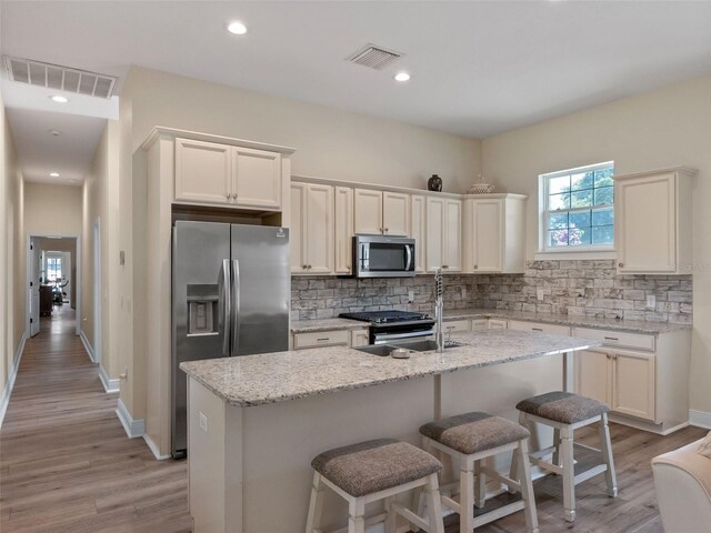 20199 Sweetwood Ln, Clermont, FL 34715 - kitchen with stainless steel appliances, decorative backsplash, light wood-style floors, a center island with sink, and white cabinets