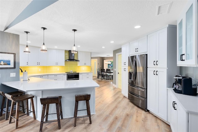 5370 Whispering Pine Cir, Saint Cloud, FL 34771 - kitchen featuring stainless steel appliances, wall chimney range hood, a breakfast bar area, a peninsula, and a textured ceiling