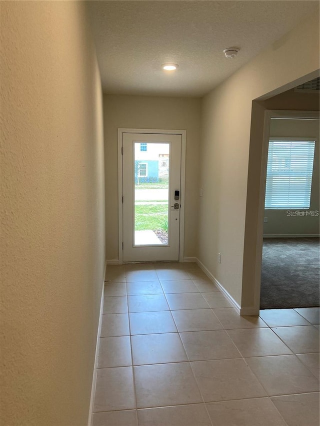 doorway with light tile patterned flooring, baseboards, a textured ceiling, and light colored carpet