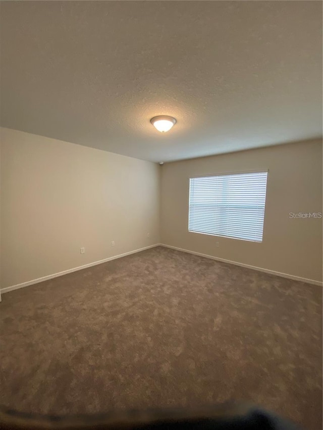 empty room with dark colored carpet and baseboards