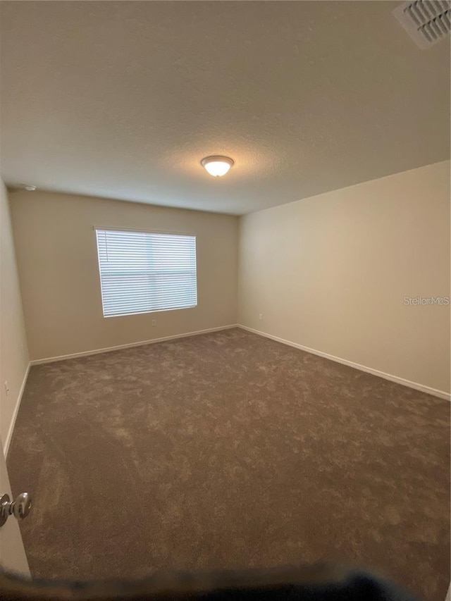 empty room featuring dark colored carpet and baseboards