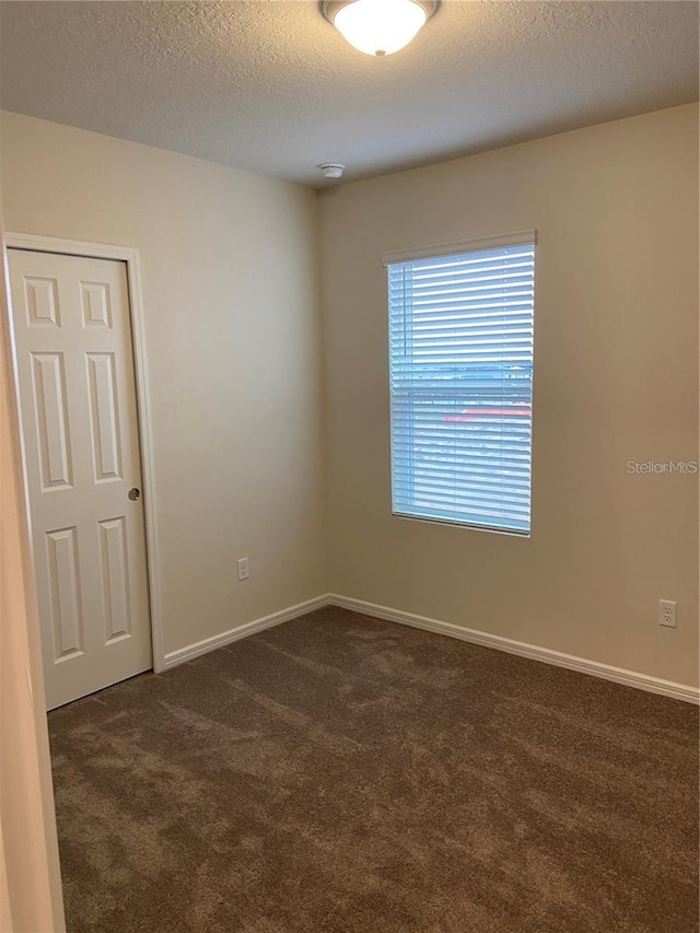 unfurnished room with dark colored carpet, a textured ceiling, and baseboards