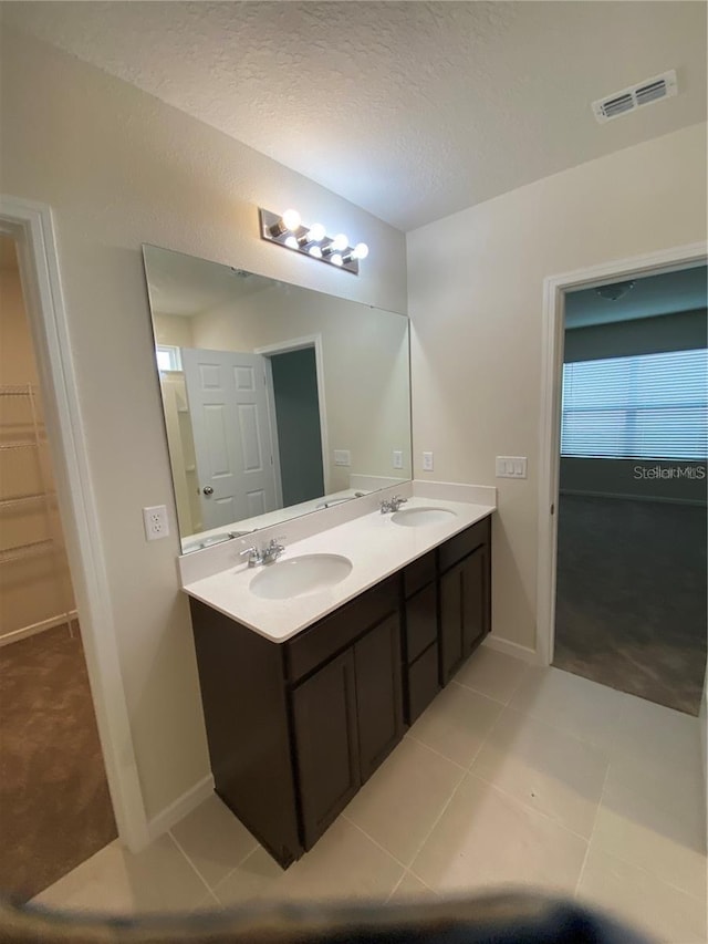 bathroom featuring double vanity, baseboards, tile patterned flooring, a textured ceiling, and a walk in closet