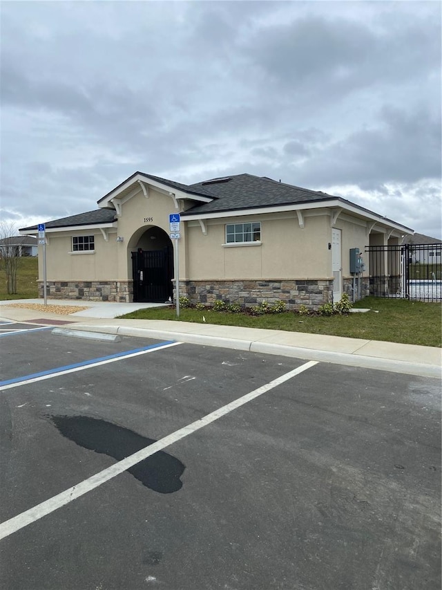 view of front of house with stucco siding, uncovered parking, stone siding, and a shingled roof