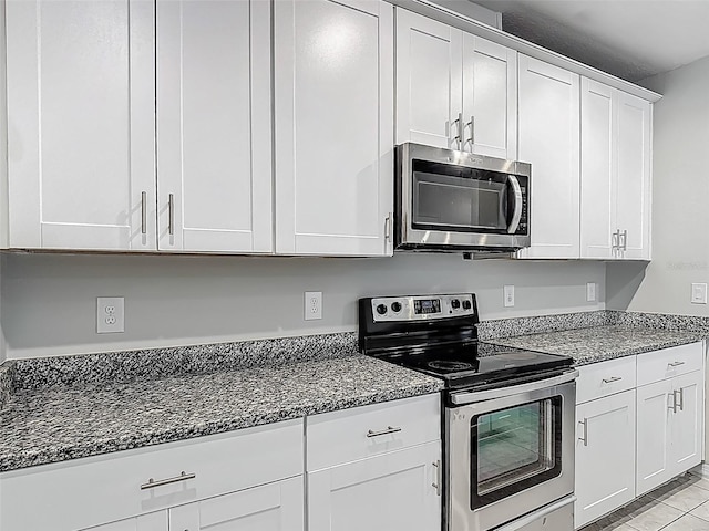 kitchen featuring appliances with stainless steel finishes, dark stone countertops, and white cabinetry