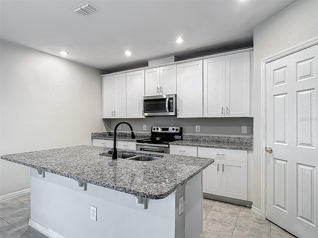 kitchen featuring stainless steel appliances, a sink, a kitchen bar, dark stone countertops, and recessed lighting