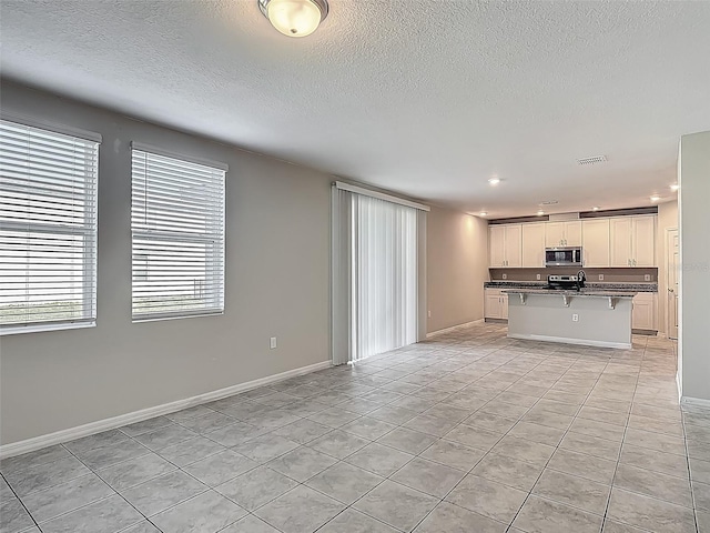 unfurnished living room with light tile patterned floors, a textured ceiling, recessed lighting, baseboards, and a sink