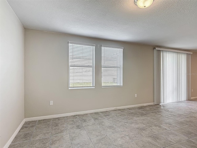 empty room with a textured ceiling, light tile patterned floors, and baseboards