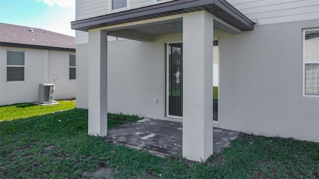 entrance to property with central AC unit, a patio, a lawn, and stucco siding