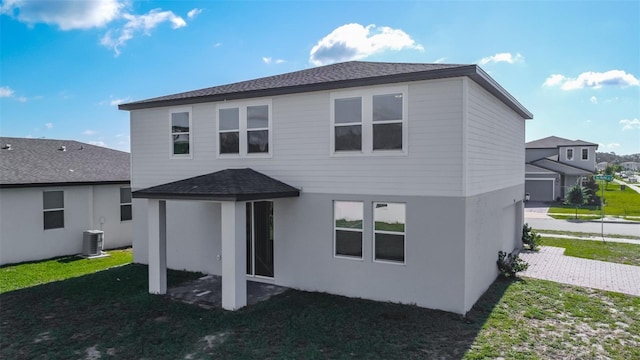 back of property with central AC unit, a shingled roof, a lawn, and stucco siding