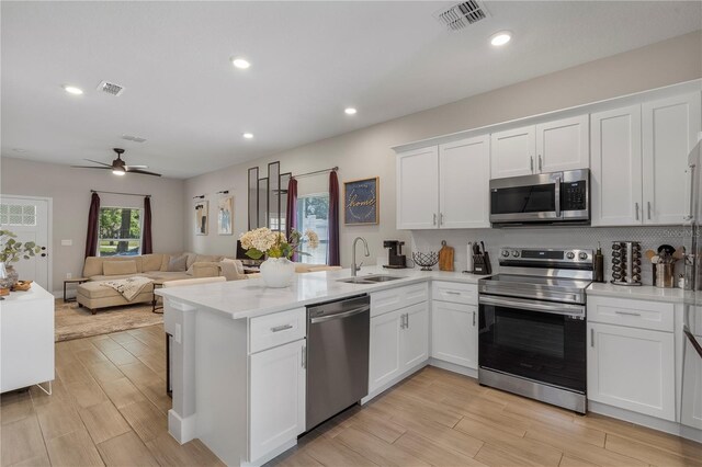 146 E 15th St, Apopka, FL 32703 - kitchen with stainless steel appliances, a sink, a peninsula, white cabinetry, and light wood-style flooring