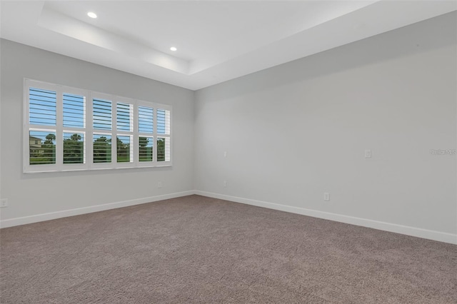 empty room featuring a raised ceiling, carpet floors, recessed lighting, and baseboards