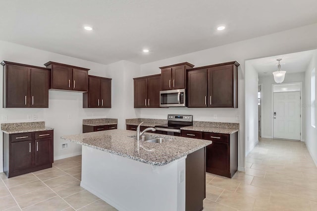 3975 Kennebunk Loop, Mount Dora, FL 32757 - kitchen featuring stainless steel appliances, light stone countertops, a kitchen island with sink, baseboards, and dark brown cabinets