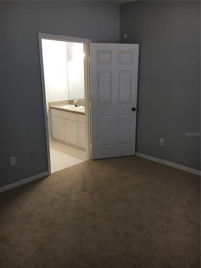 unfurnished bedroom featuring a sink, light carpet, ensuite bathroom, and baseboards