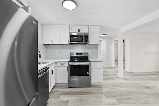 4119 Beacon Square Dr, Holiday, FL 34691 - kitchen featuring stainless steel appliances, a sink, light countertops, white cabinets, and light wood finished floors