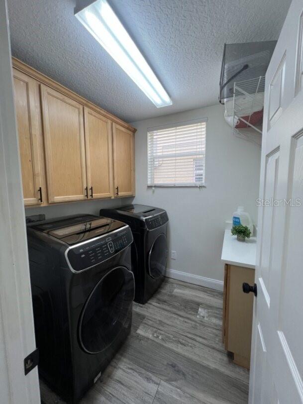 14936 Masthead Landing Cir, Winter Garden, FL 34787 - washroom featuring washing machine and dryer, cabinet space, a textured ceiling, light wood-style flooring, and baseboards