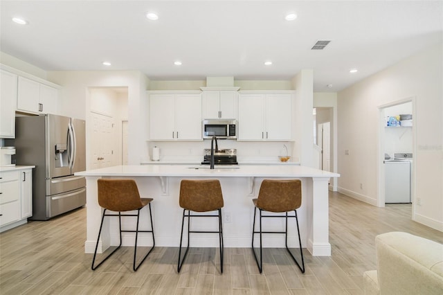 14655 Erice Ave, Clermont, FL 34714 - kitchen featuring stainless steel appliances, washer / dryer, light wood-type flooring, a center island with sink, and recessed lighting