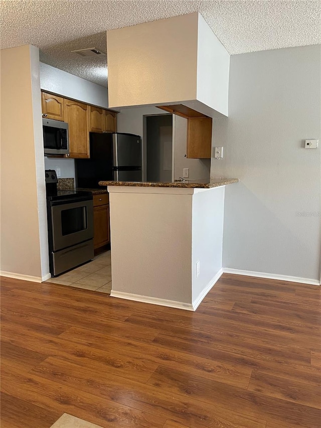 238 Afton Sq Unit 204, Altamonte Springs, FL 32714 - kitchen featuring stainless steel appliances, dark countertops, a textured ceiling, light wood-style flooring, and a peninsula