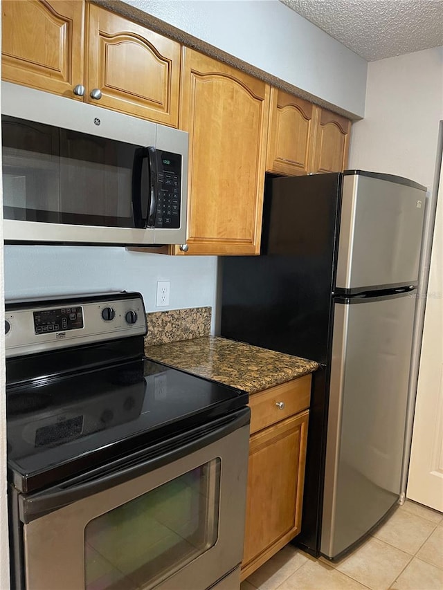 238 Afton Sq Unit 204, Altamonte Springs, FL 32714 - kitchen with appliances with stainless steel finishes, light tile patterned floors, a textured ceiling, dark stone counters, and brown cabinets
