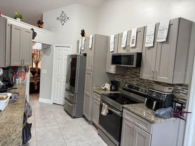 2514 Dovetail Dr, Ocoee, FL 34761 - kitchen with stainless steel appliances, decorative backsplash, light tile patterned flooring, gray cabinetry, and light stone counters