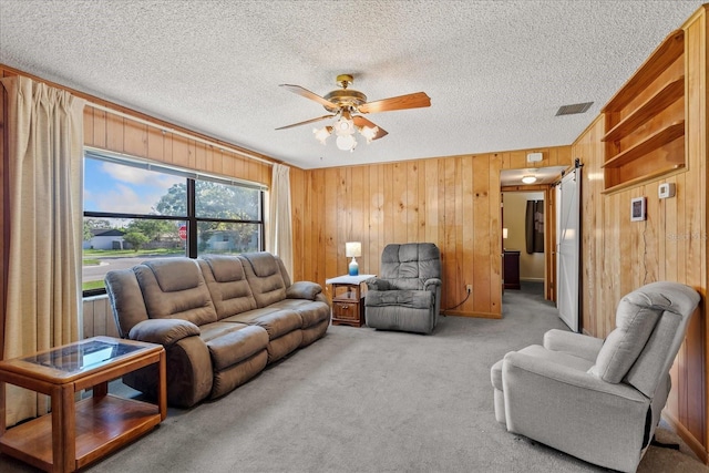 living room featuring ceiling fan, carpet flooring, wood walls, and a textured ceiling