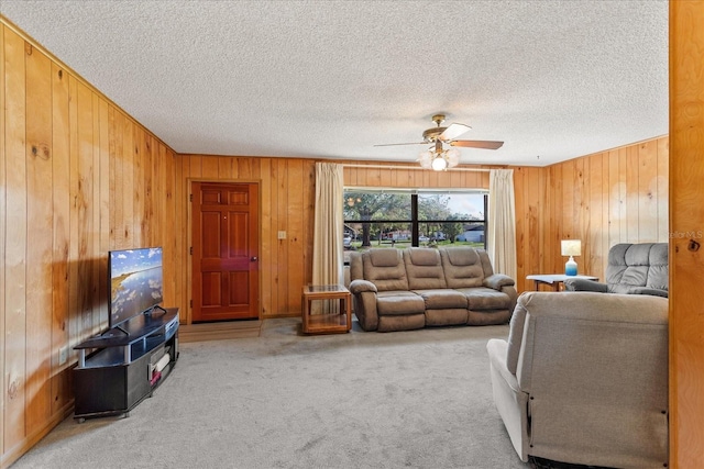 living area featuring wood walls, a ceiling fan, carpet floors, and a textured ceiling