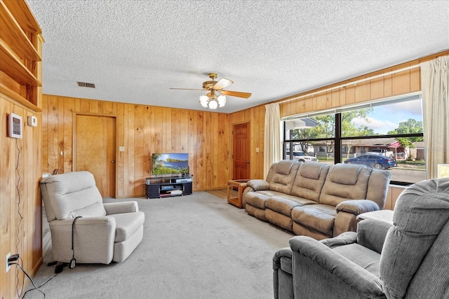 living area with light carpet, wood walls, a ceiling fan, and a textured ceiling