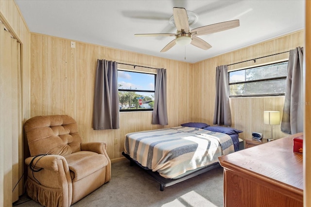 carpeted bedroom featuring wood walls and a ceiling fan