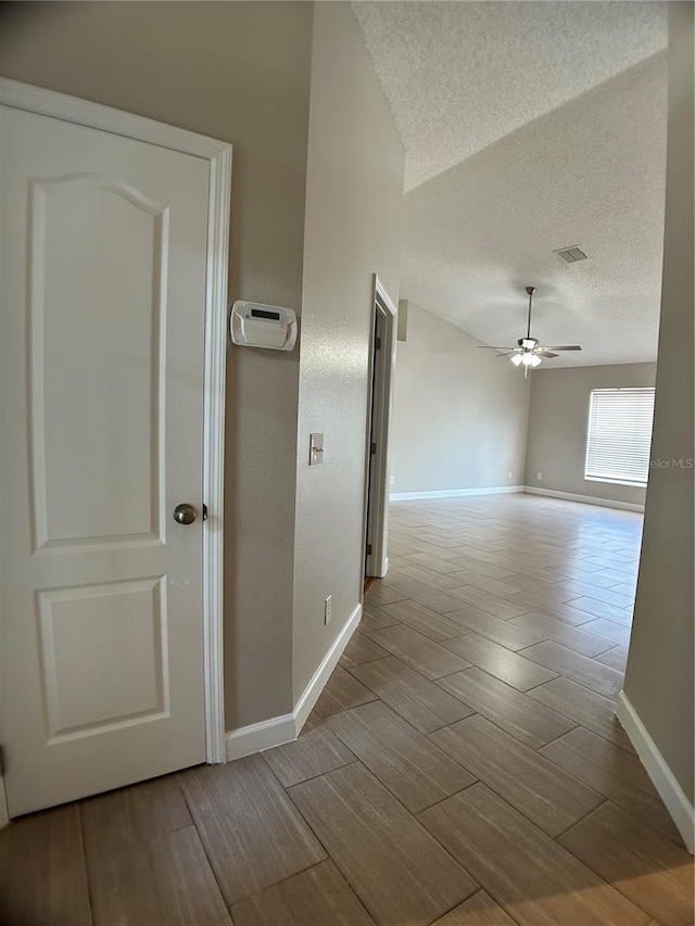corridor featuring a textured ceiling, wood finished floors, and baseboards