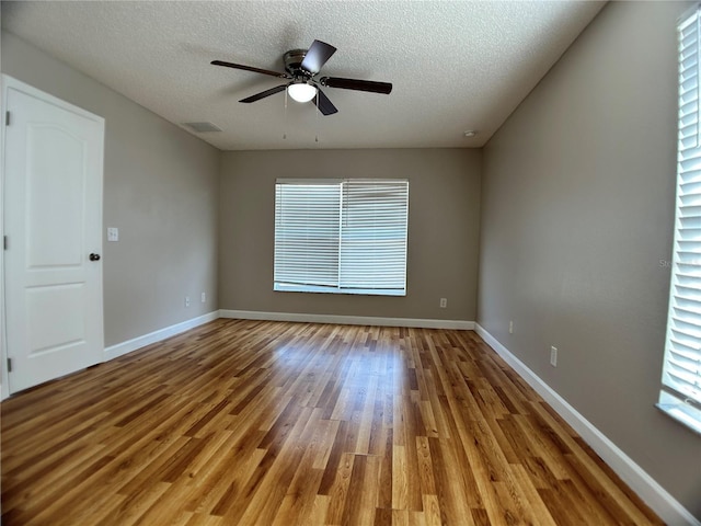 empty room featuring a textured ceiling, wood finished floors, ceiling fan, and baseboards